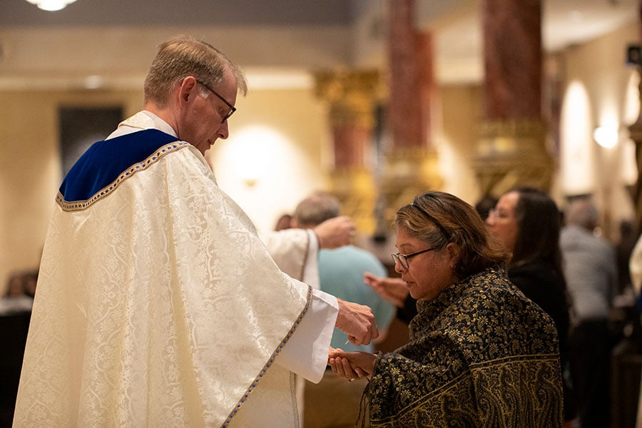 A priest presents the Eucharist to a parishioner